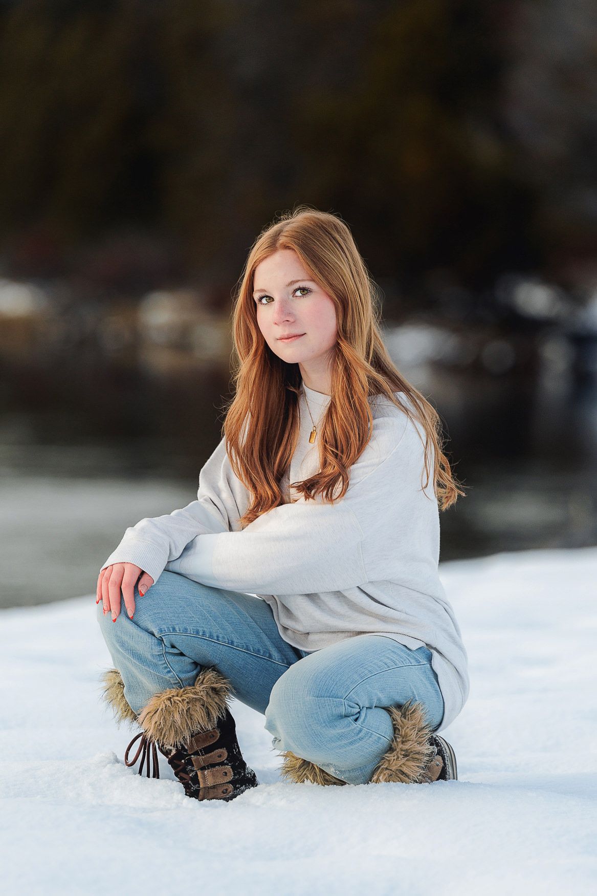 Winter outdoor portrait of someone in white sweater and jeans sitting in snow.