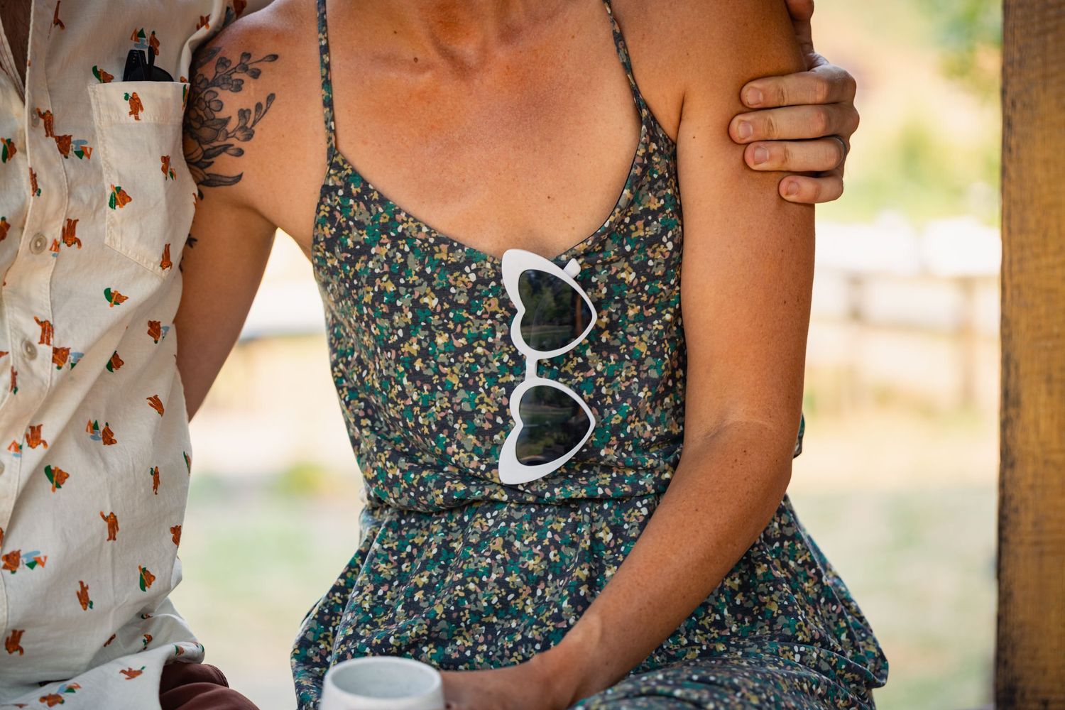 A floral sundress with white heart-shaped sunglasses hanging from the neckline on a summer day.