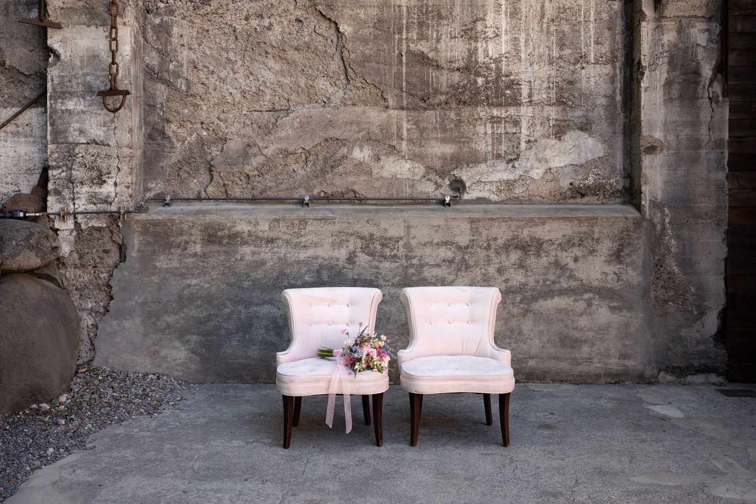 Two vintage pink armchairs sitting against a weathered concrete wall in an industrial setting.