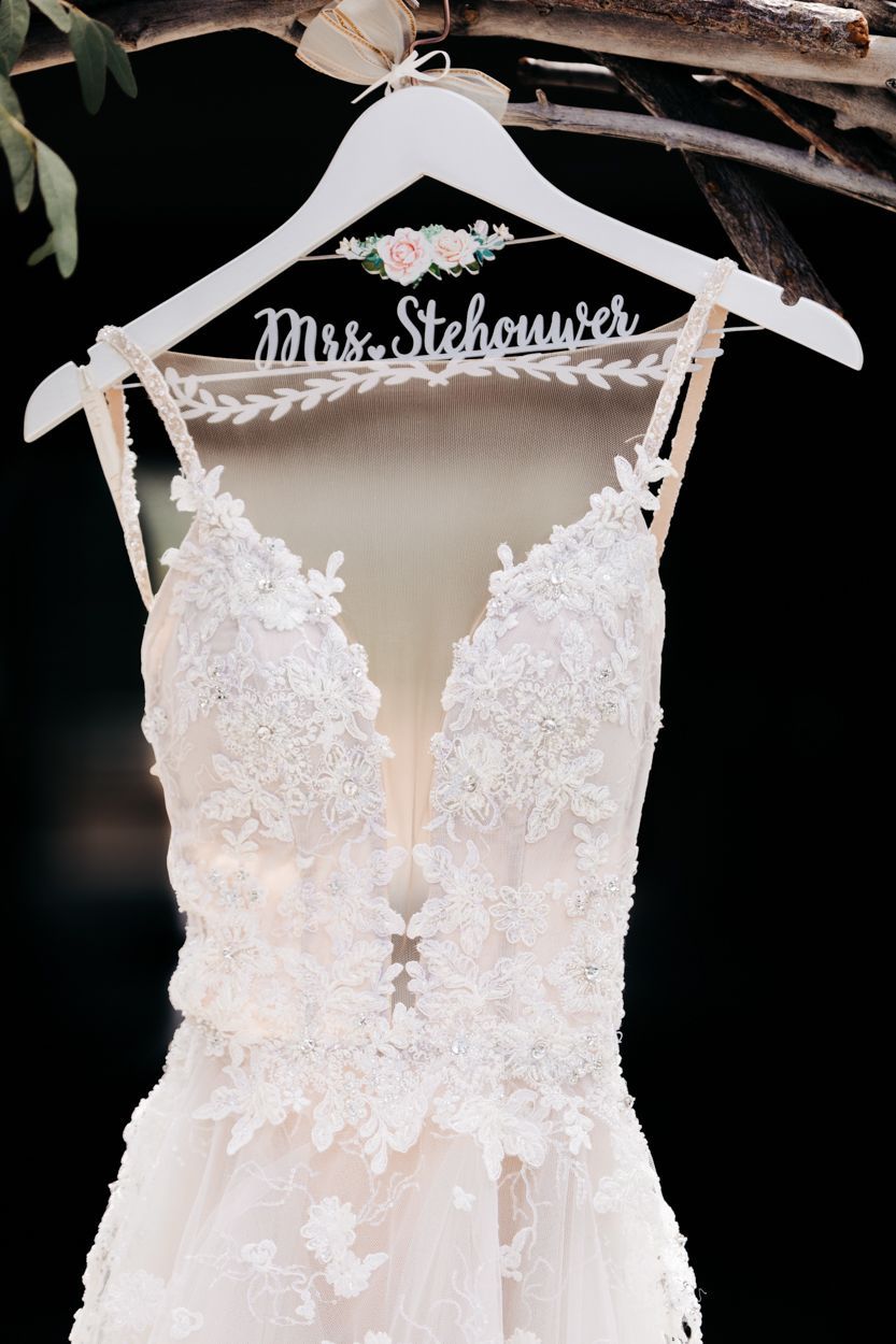 Elegant white lace wedding dress with plunging neckline hanging on personalized hanger with delicate floral embellishments.
