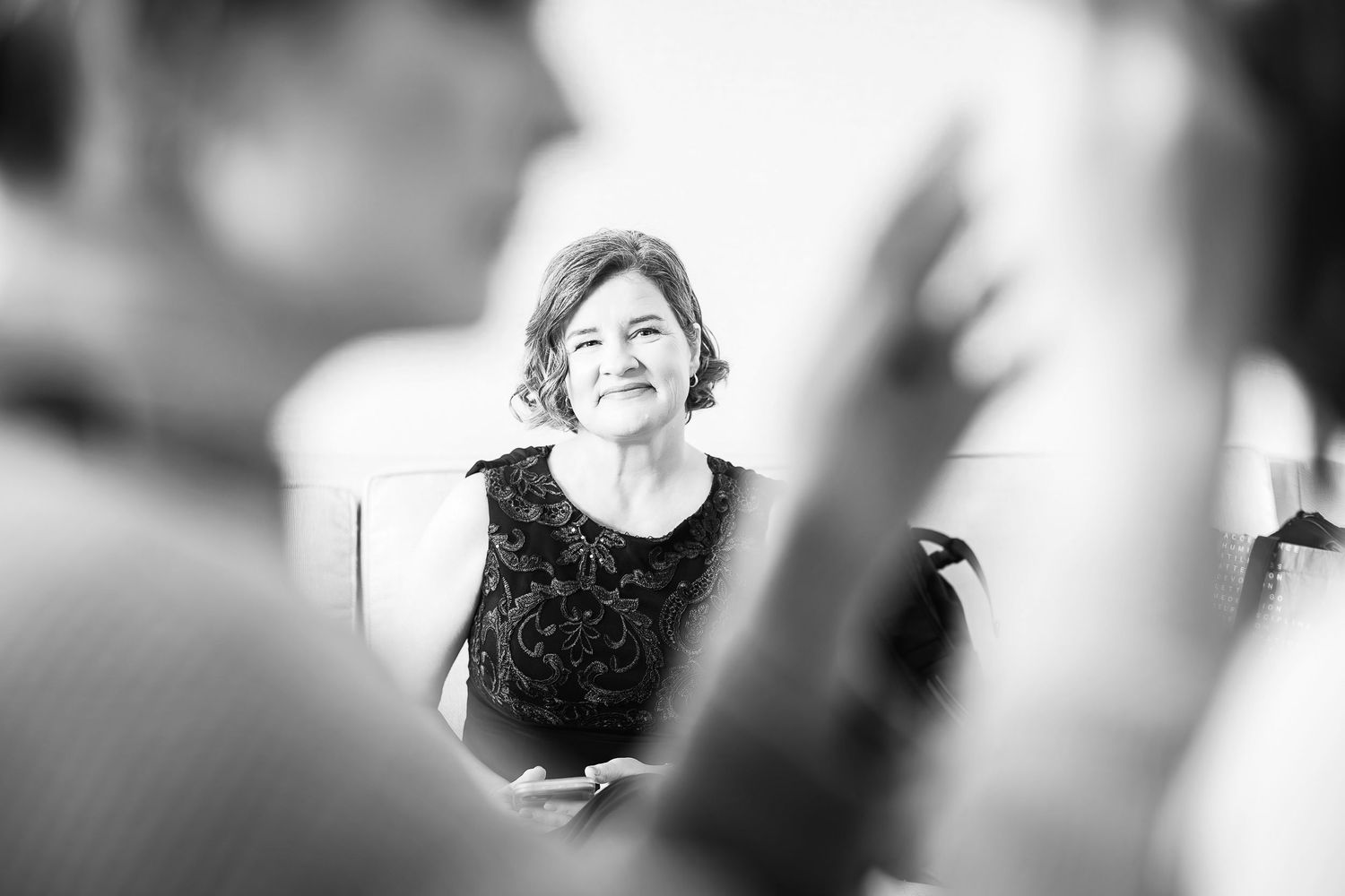 Black and white candid photo showing a person in a dark sleeveless dress smiling during what appears to be a social gathering.