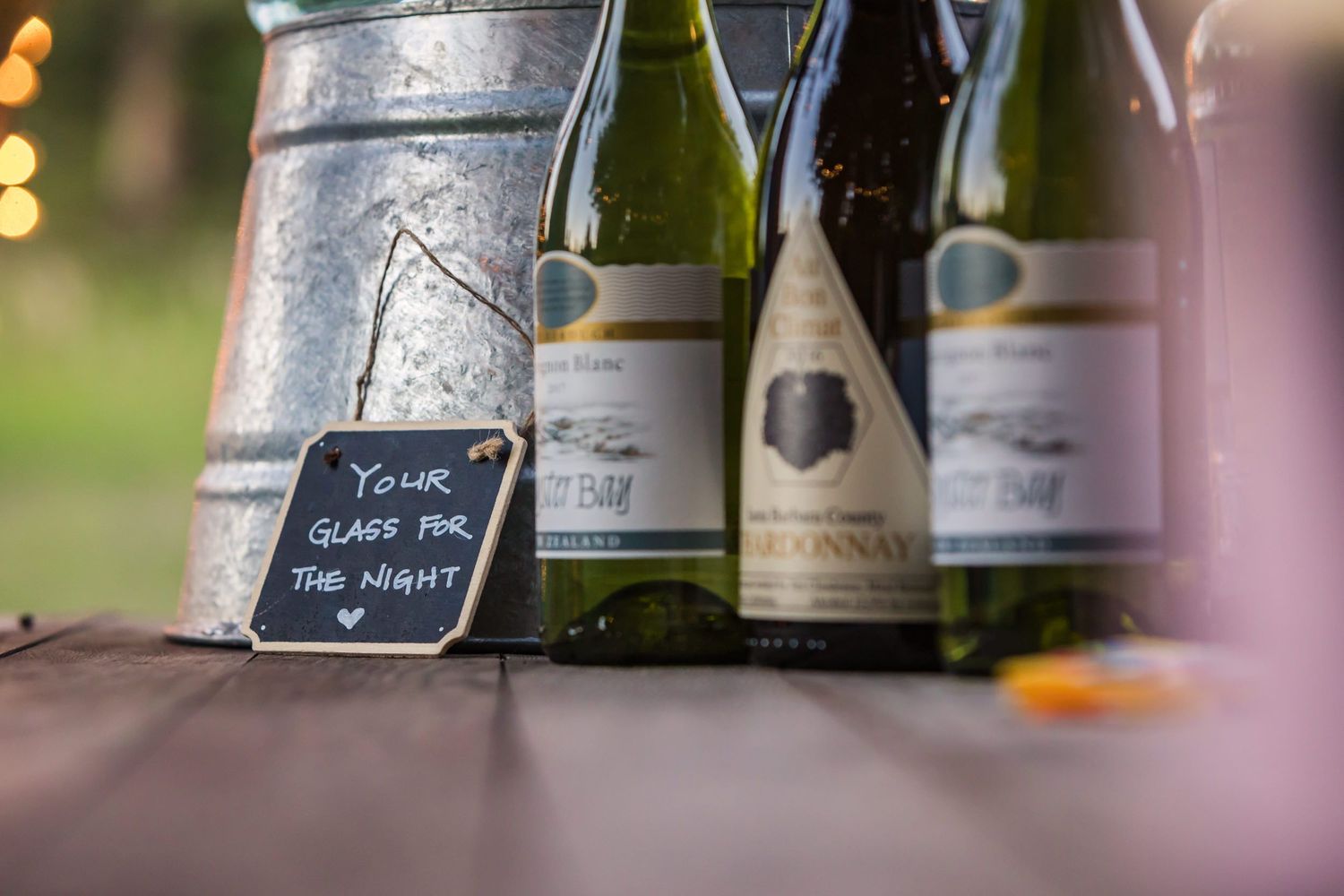 Wine bottles and keg displayed on rustic table with handwritten sign.
