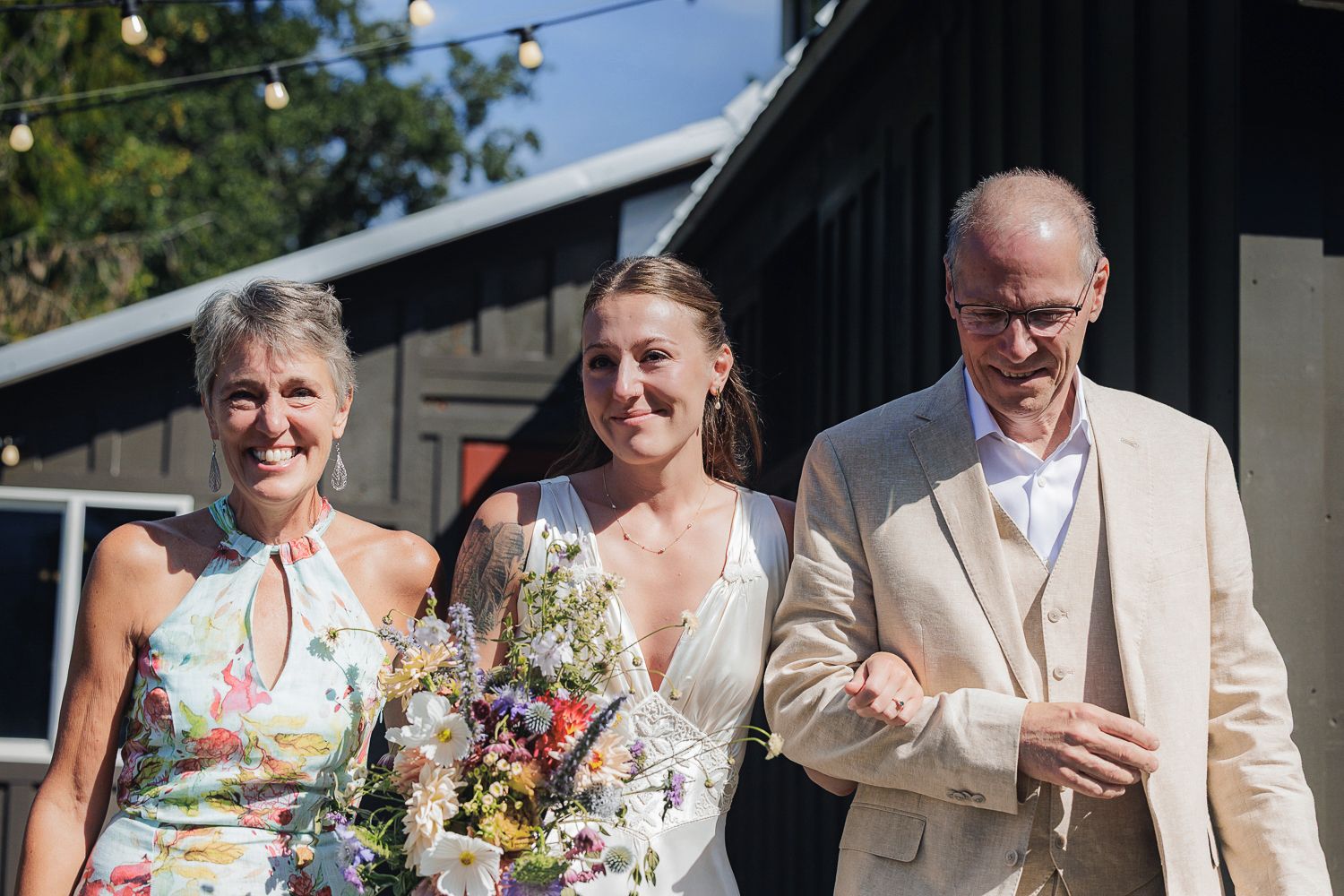 Wedding party members smile together outdoors during a summer celebration with floral bouquets.