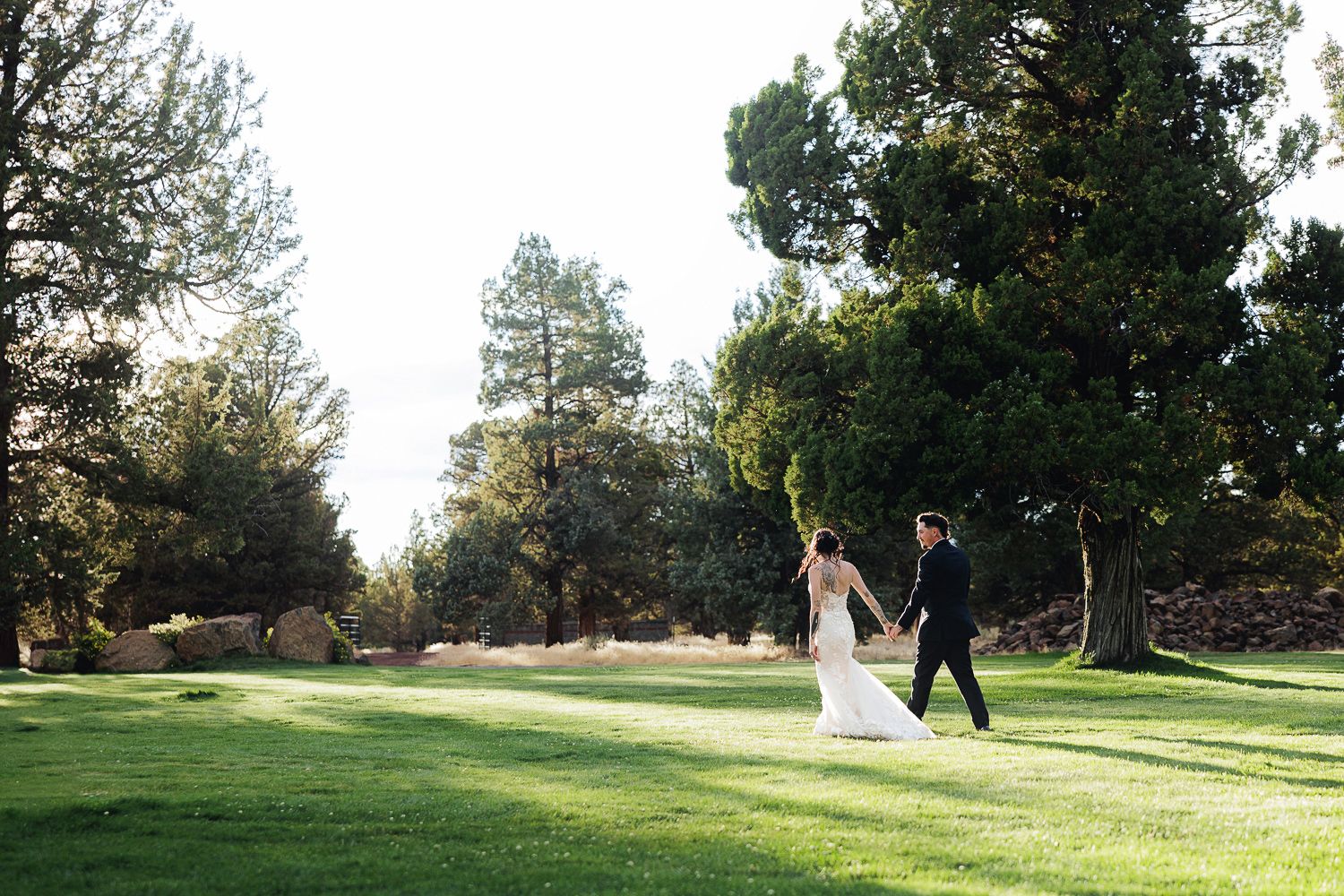 A couple walks joyfully across a lush green golf course surrounded by tall trees at golden hour.