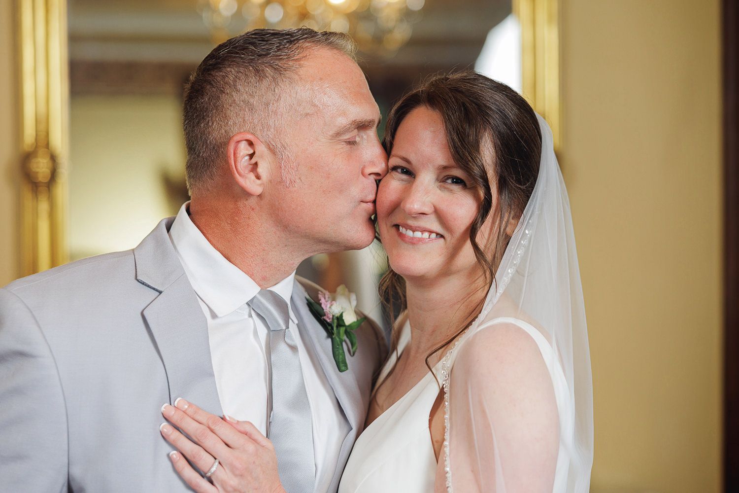 Wedding couple shares an intimate moment in front of an elegant gold paneled wall with a crystal chandelier.