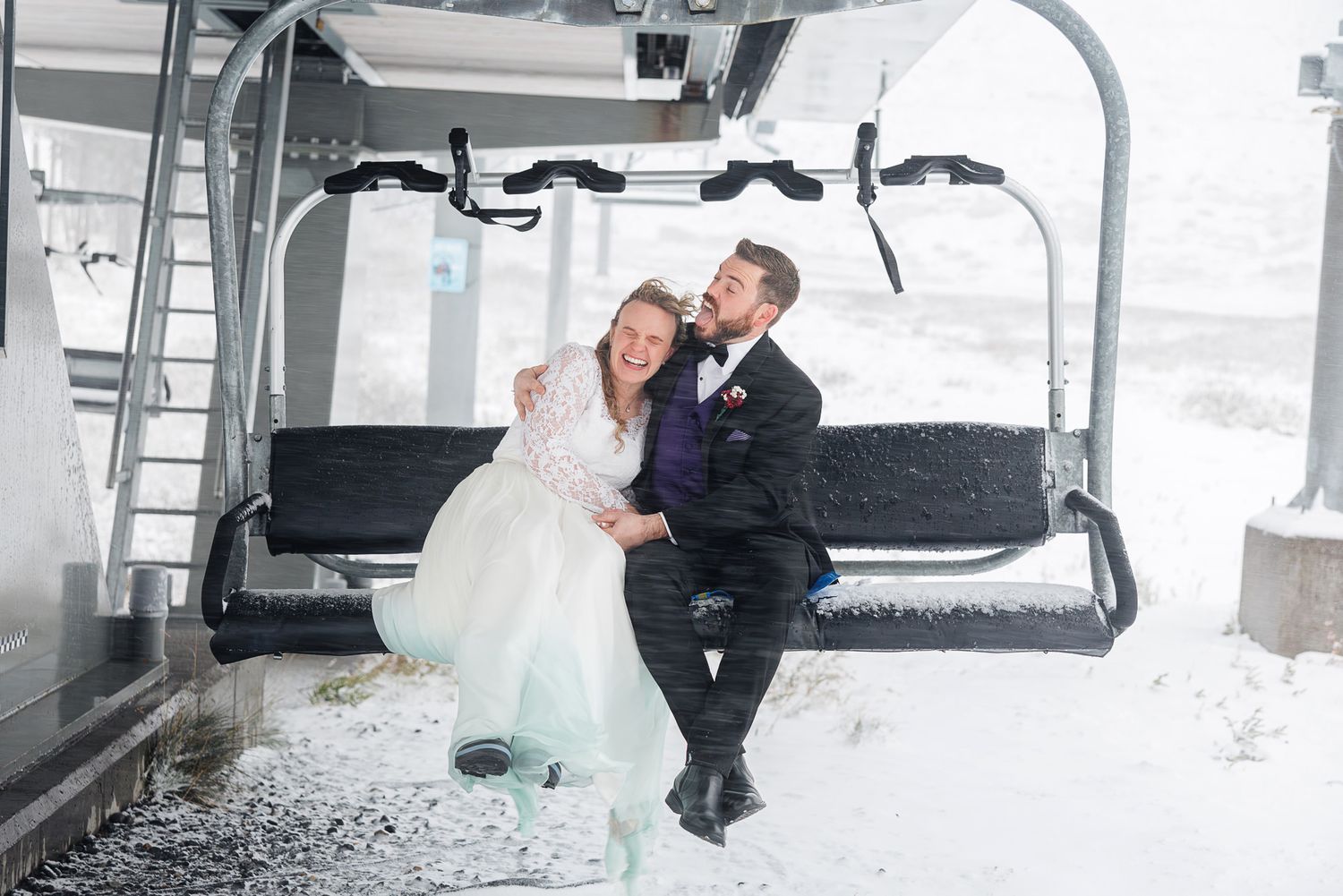 A couple in wedding attire shares an intimate moment while sitting in a ski lift gondola on a snowy winter day.