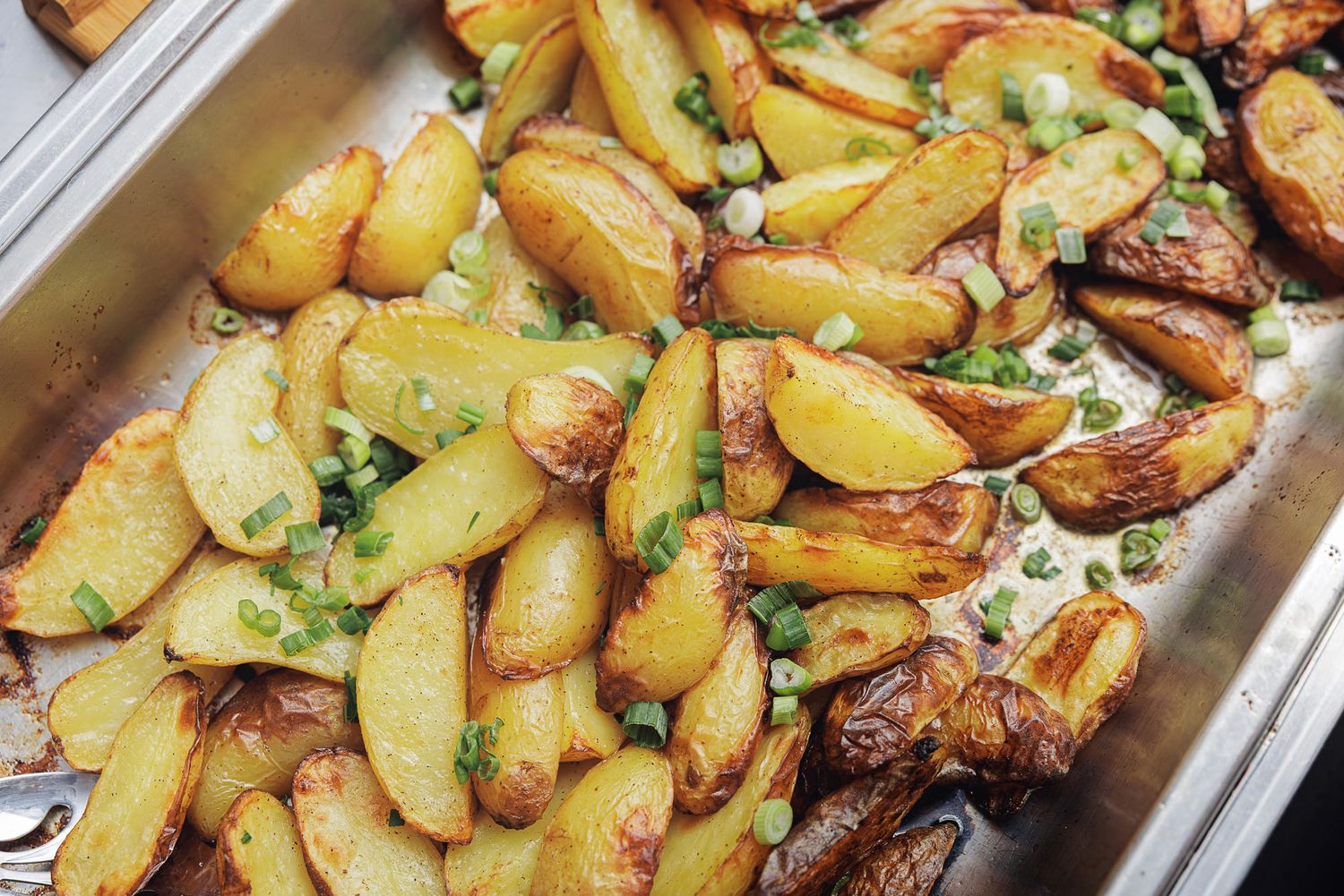 Golden roasted potato wedges garnished with fresh herbs on a white serving platter.