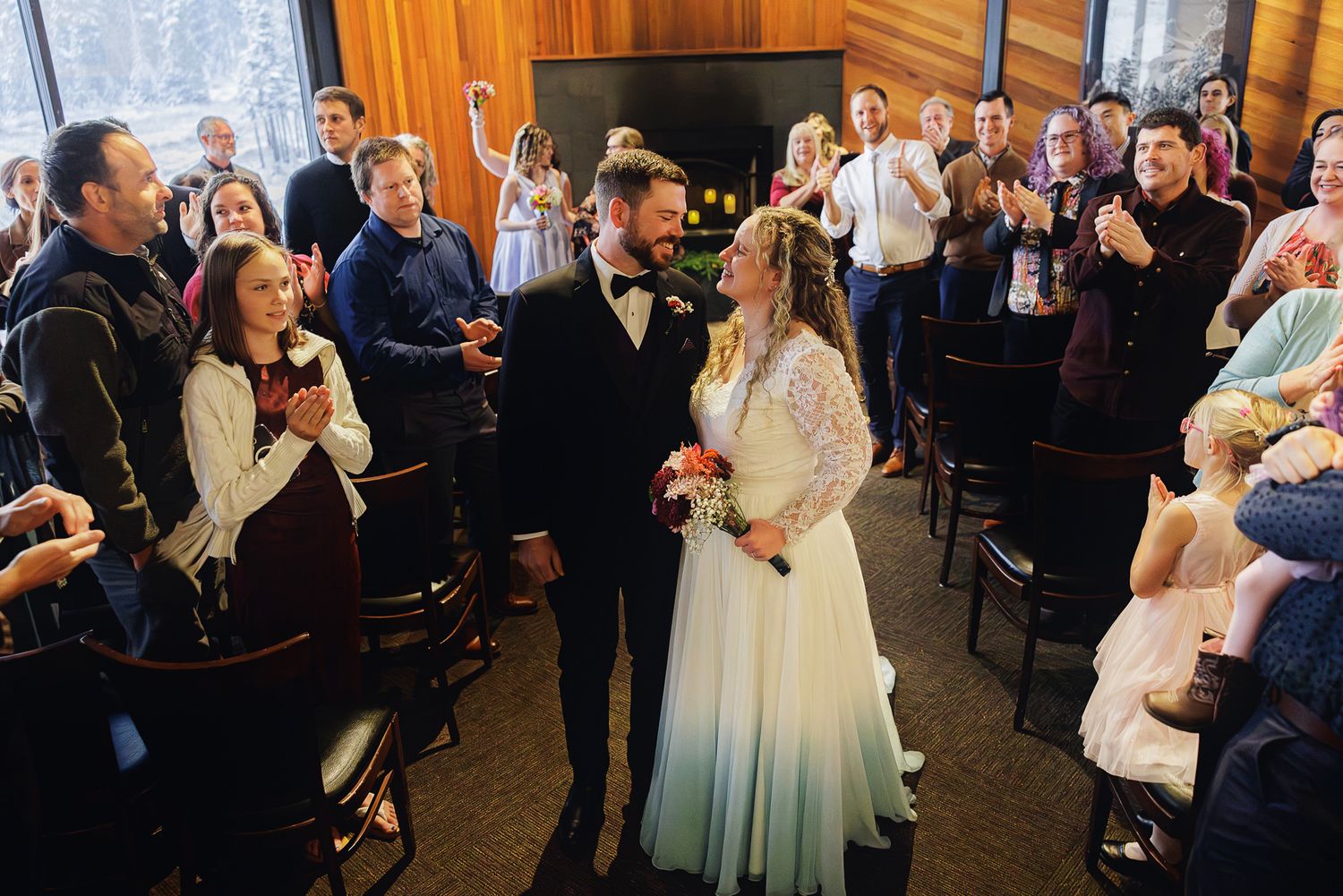 Wedding guests gather in an elegant indoor venue with warm lighting and wooden paneled walls during a celebration.