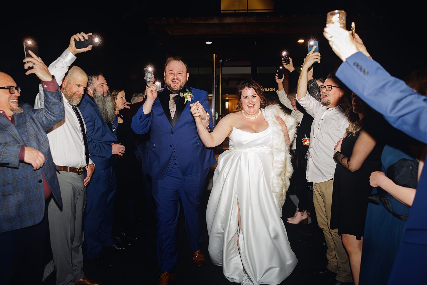 A group of wedding guests dance together in a celebratory circle on a dimly lit dance floor.