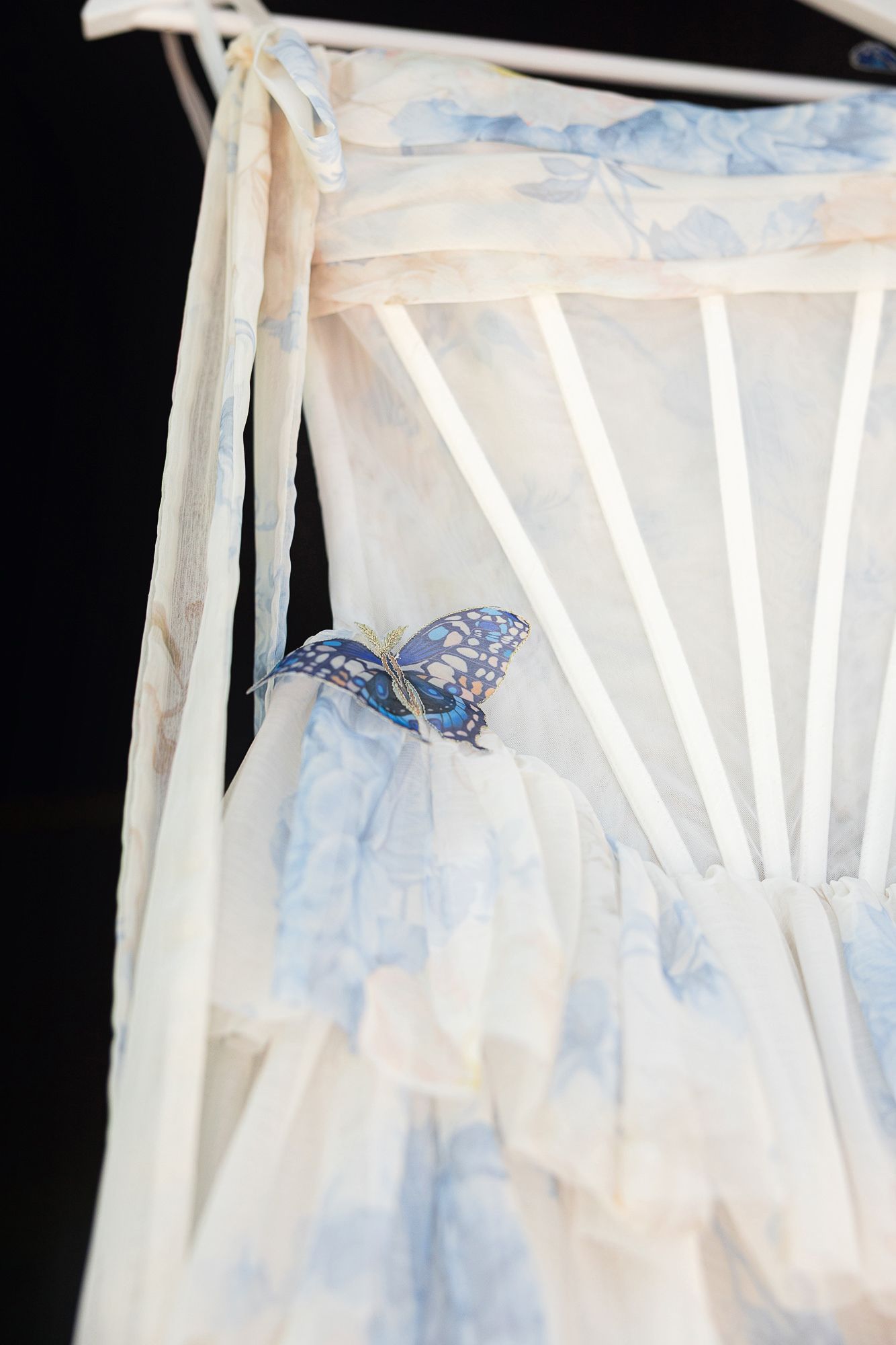 Blue floral chiffon dress with boned corset bodice and butterfly brooch detail on a hanger.