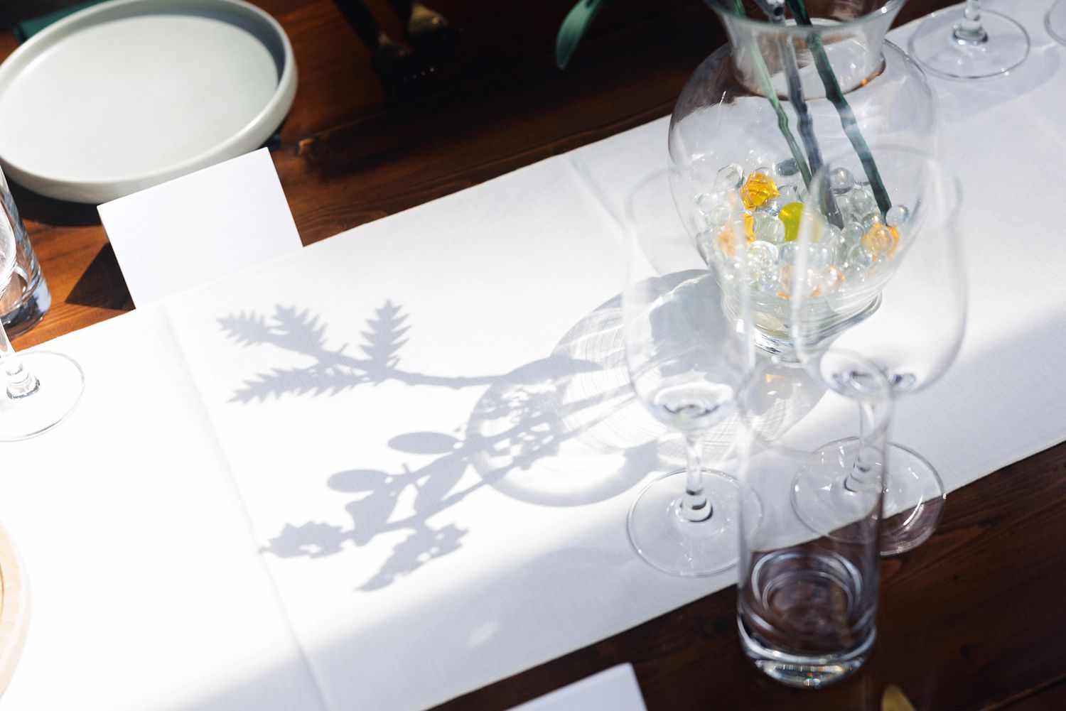 Elegant white table runner with floral shadow pattern, wine glasses, and a floral centerpiece on a wooden table.