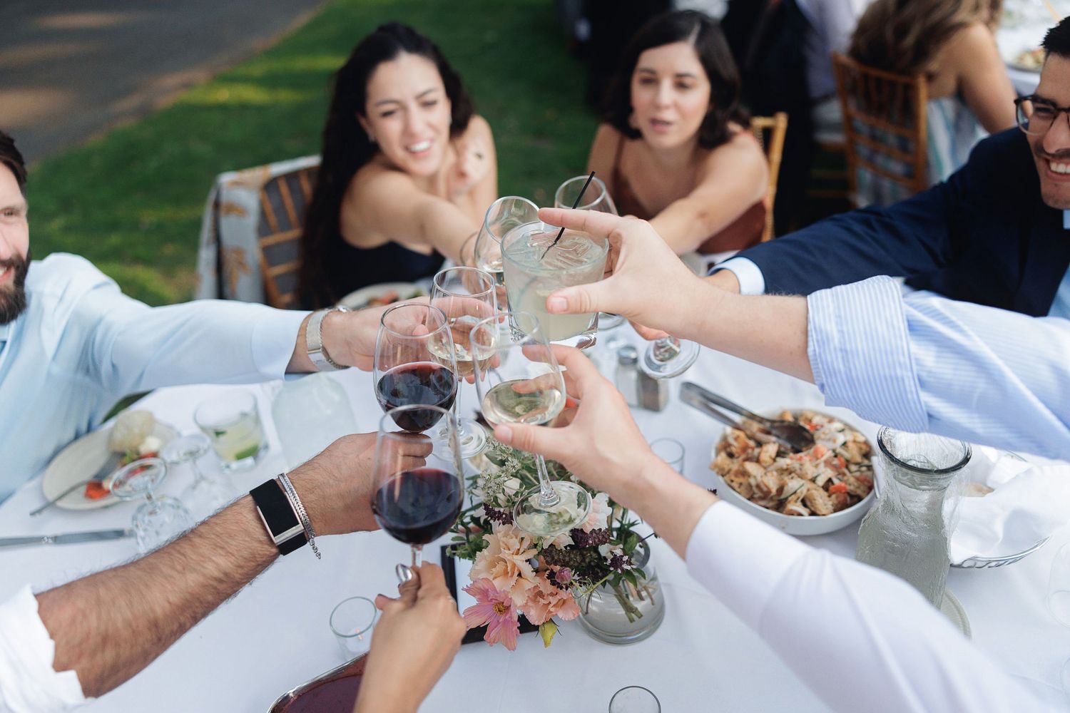 Friends toasting with wine glasses at an outdoor garden dinner party celebration.