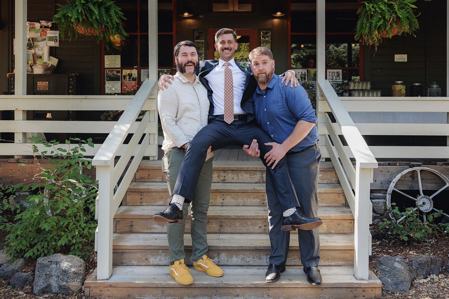 Five people smile while sitting on white wooden steps in front of a building.