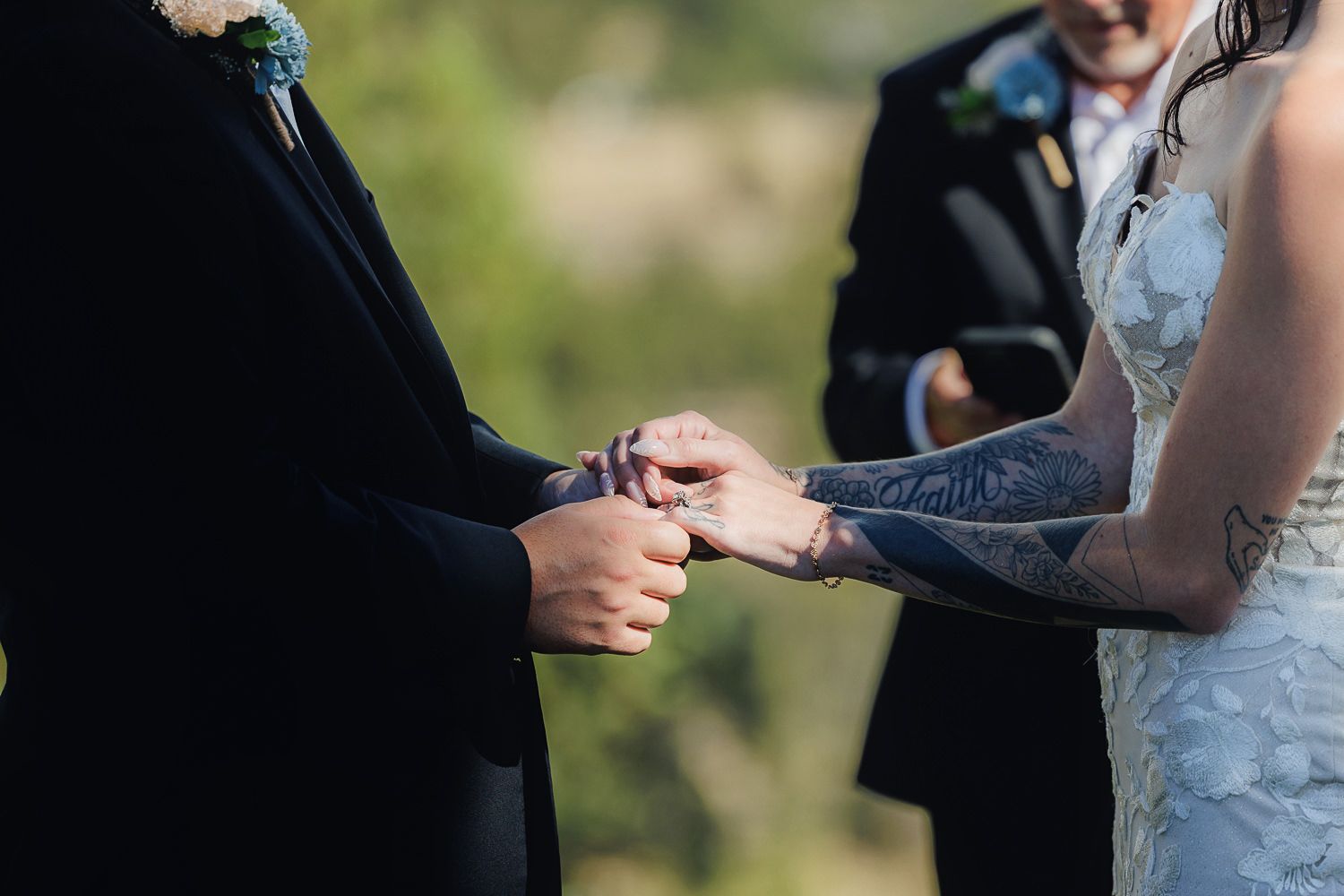 Someone exchanges rings with their partner during an outdoor wedding ceremony in natural sunlight.