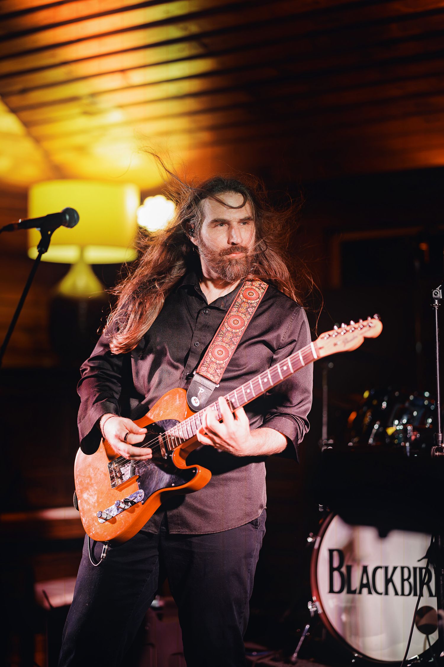 Long-haired bearded guitarist performs on stage with orange electric guitar for Blackbird band.