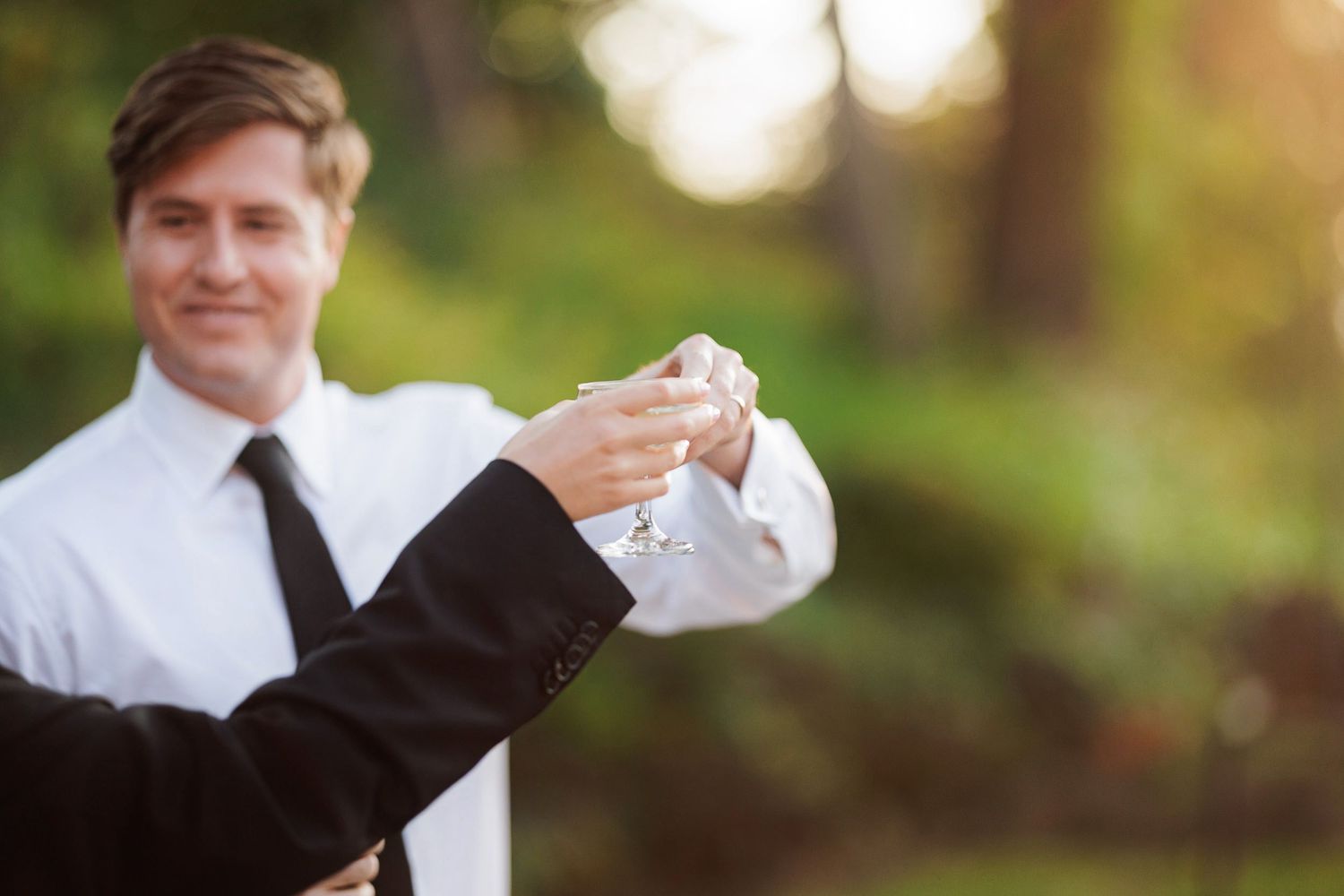 Groom in white shirt and tie having cufflinks fastened outdoors at a wedding ceremony.