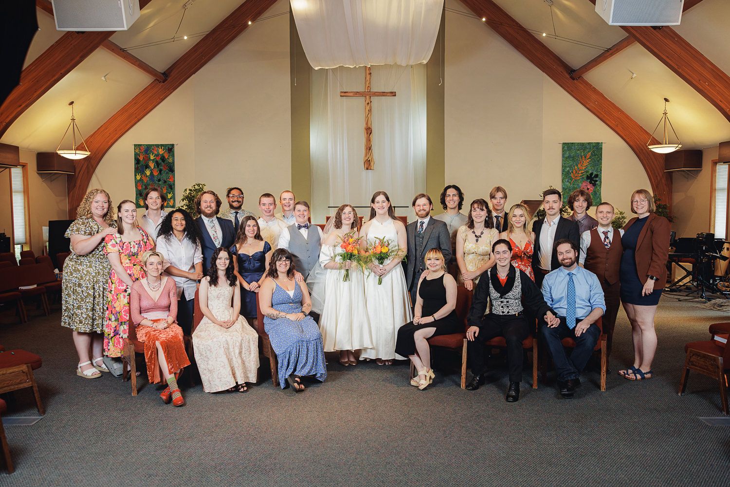 Wedding guests gather for a group photo inside a church sanctuary with wooden beams and stained glass windows.