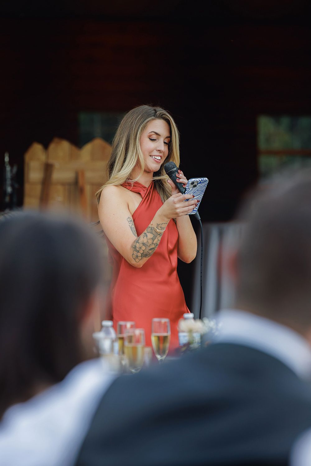 Woman in coral sleeveless top smiles while looking at mobile phone during social gathering.