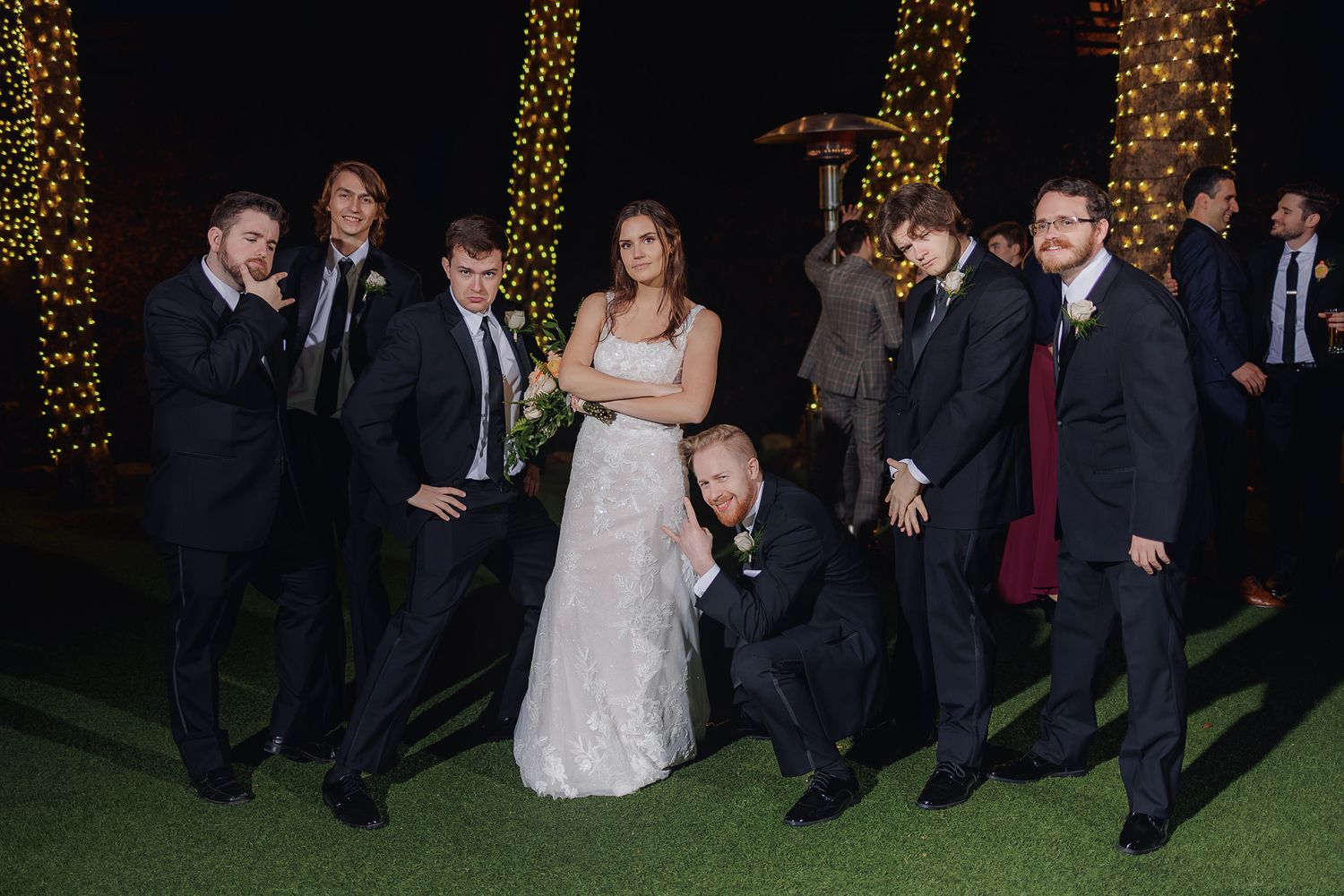Wedding party poses together at night with twinkle lights creating a festive outdoor atmosphere.