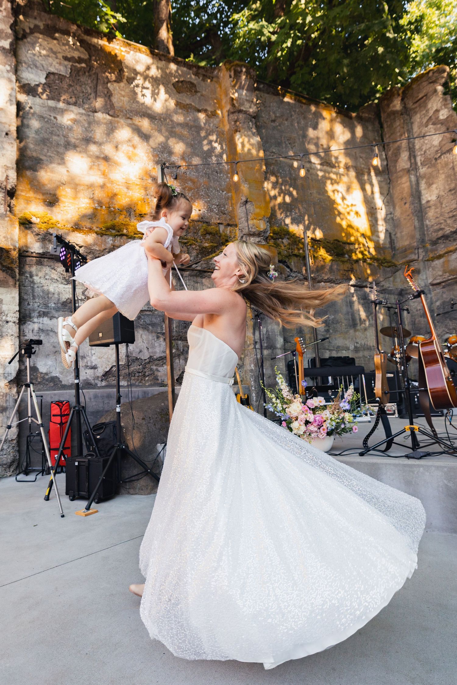 A glowing stone wall forms the backdrop for a joyful outdoor dance performance on a stage with musical instruments.