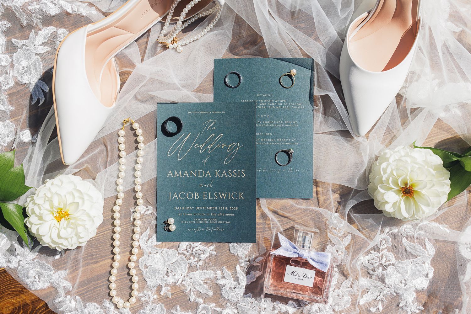 Wedding invitation suite with teal acrylic invites, white heels, pearls, perfume bottle and white flowers on lace background.