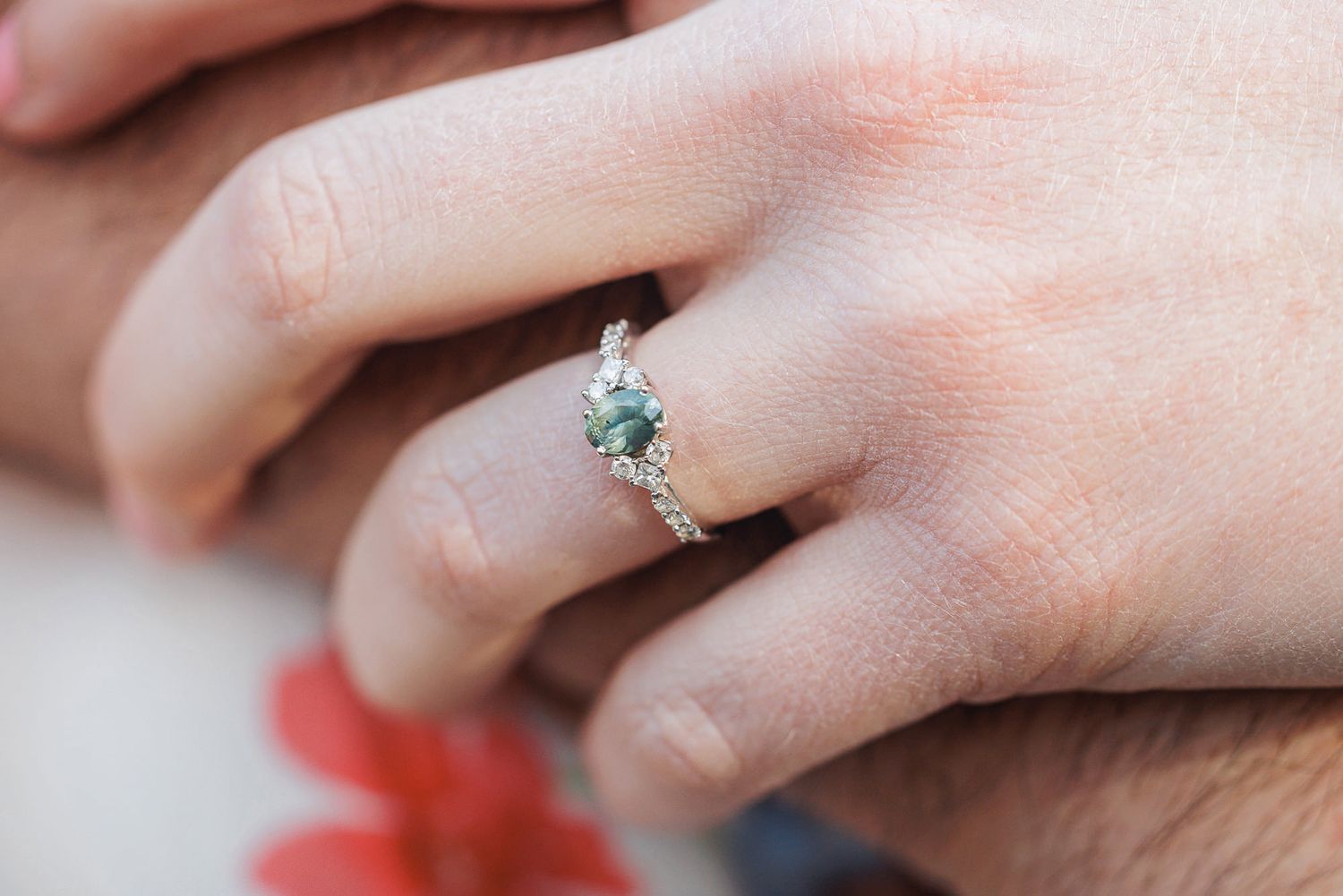 Close-up of a hand wearing a silver engagement ring with a green moss agate center stone and diamond accents.