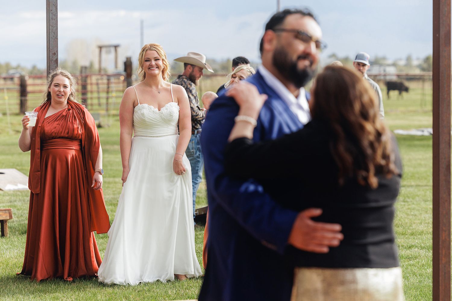 Bride in white gown smiles as couple shares first dance at rustic outdoor wedding ceremony on green lawn.