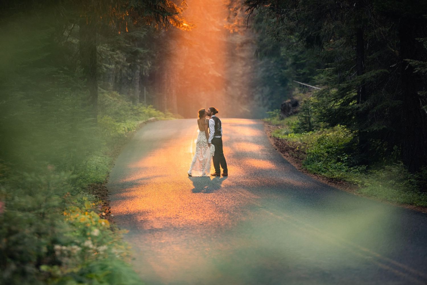 A romantic moment captured on a sunlit forest road with rays of golden light filtering through the trees.