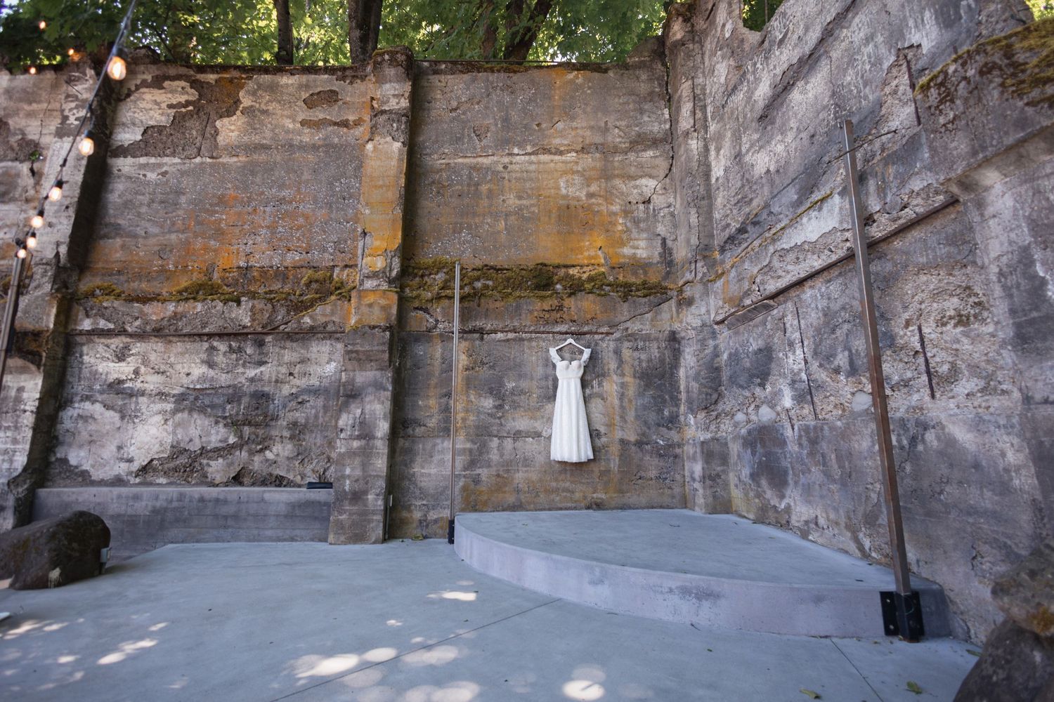 White dress hangs against tall weathered stone wall in outdoor amphitheater setting.