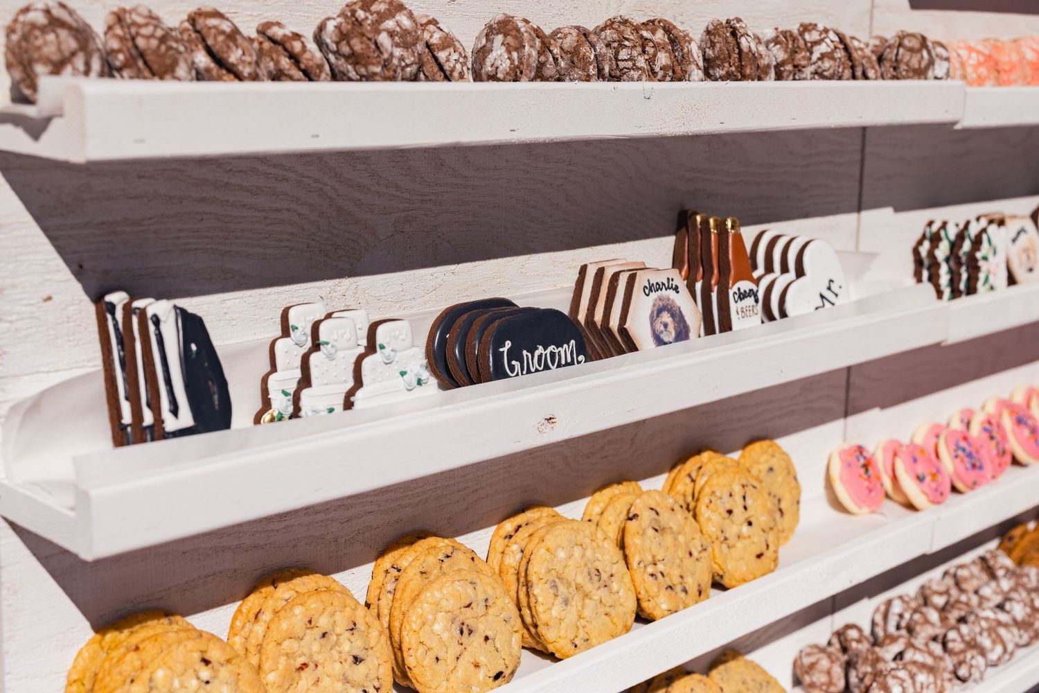 Rows of freshly baked round chocolate cookies and slices of bread displayed on white bakery shelves.
