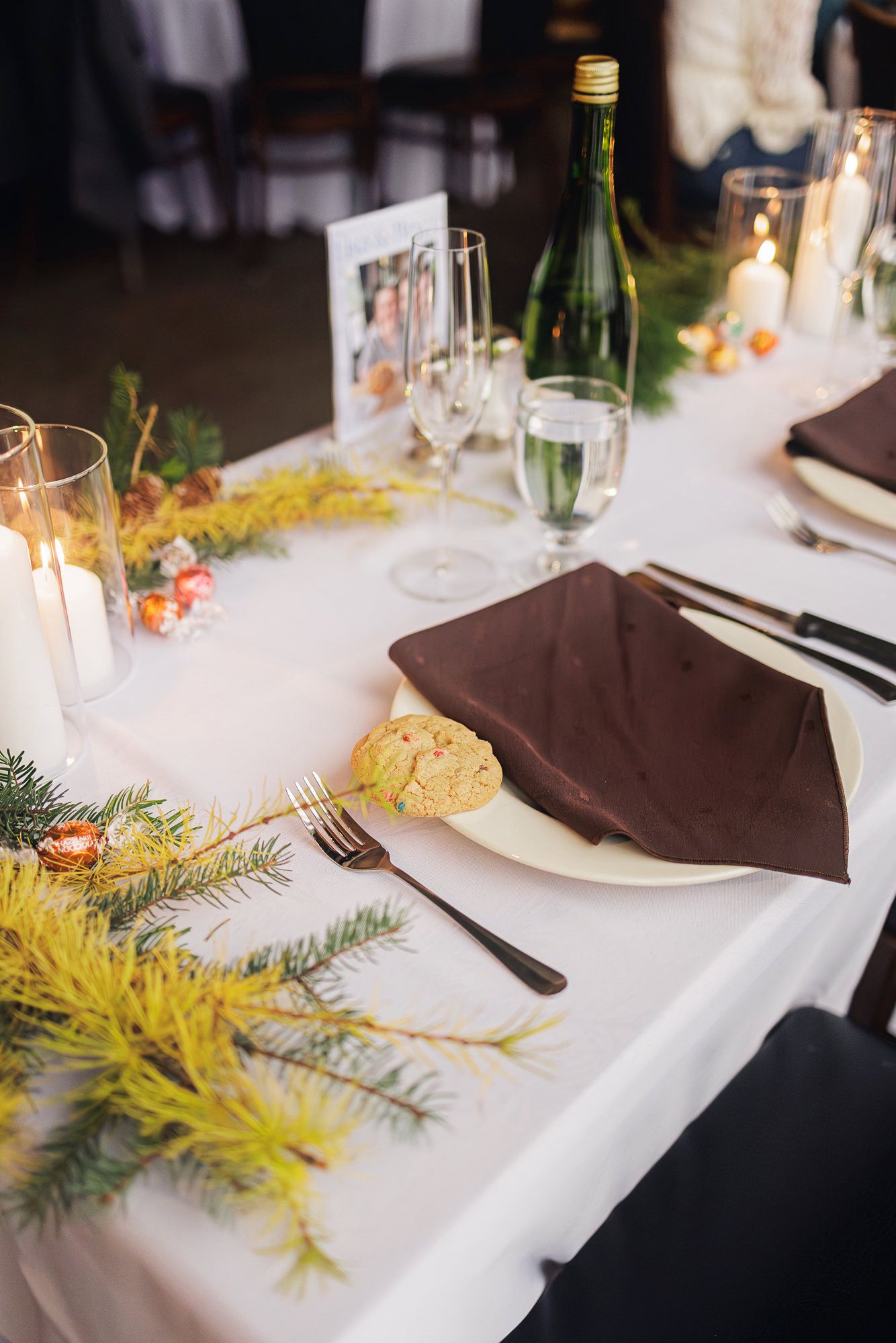 Elegant table settings with white linens, brown napkins, and evergreen sprigs create a festive holiday dining atmosphere.