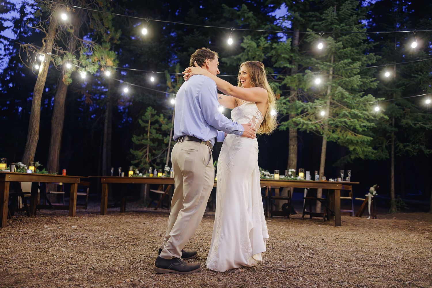 Newlyweds share a romantic dance under glowing string lights at an intimate outdoor evening wedding reception.