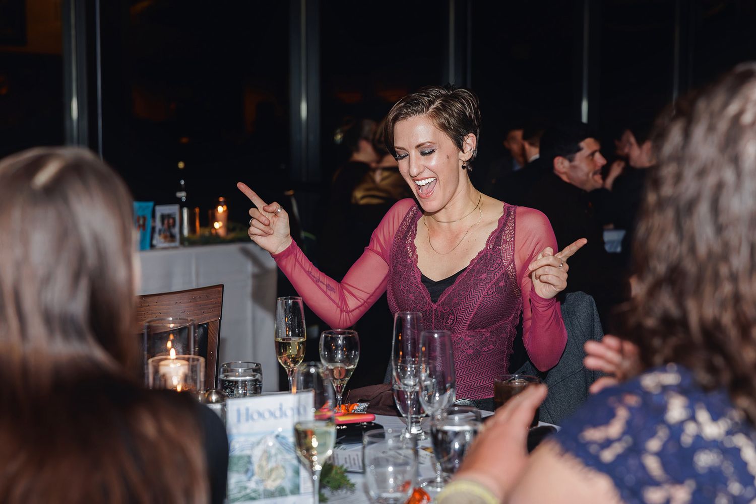 Wedding guests enjoying a lively reception dinner in a warmly lit restaurant setting.