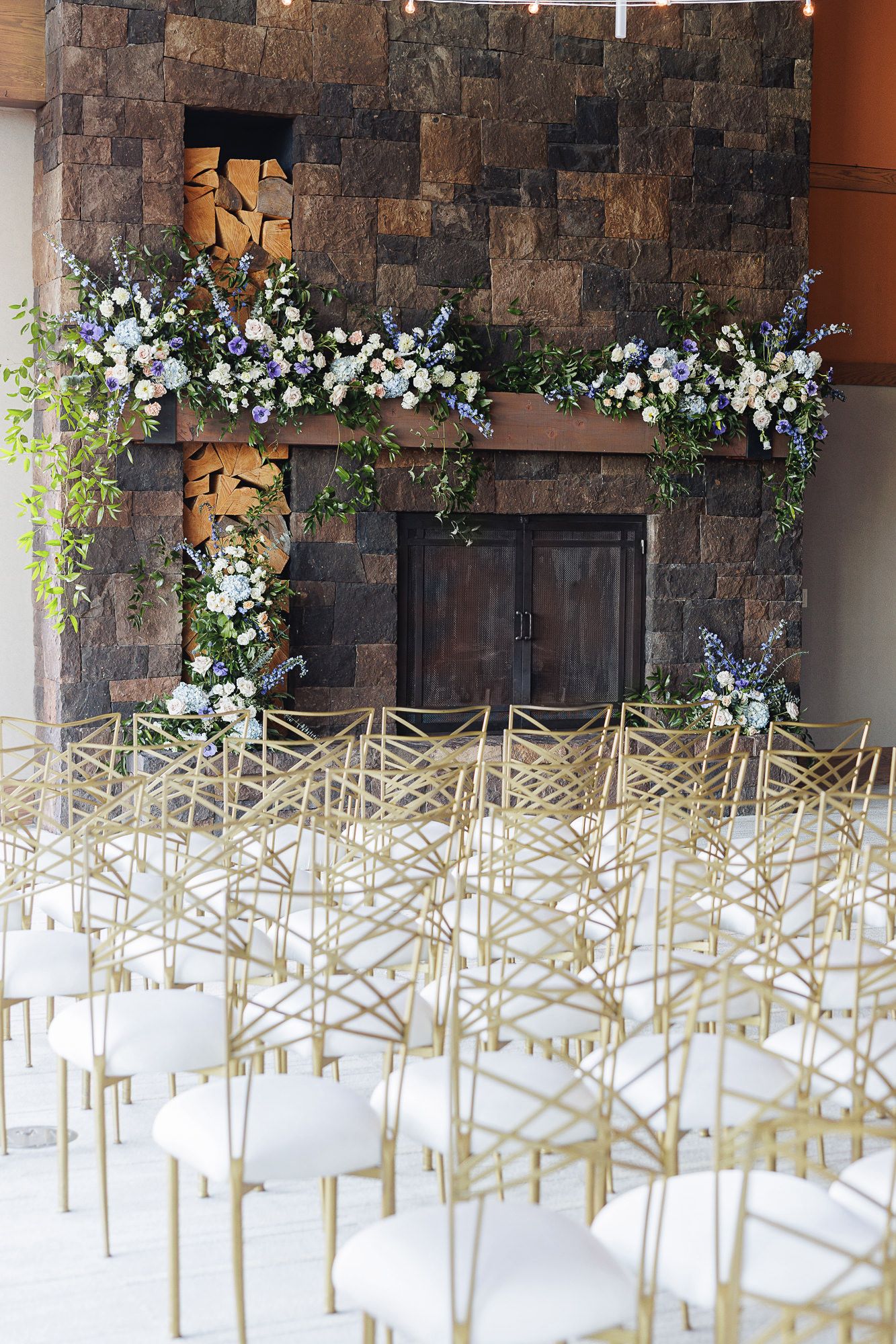 White chairs arranged in geometric pattern for outdoor wedding ceremony with stone wall and floral decorations.