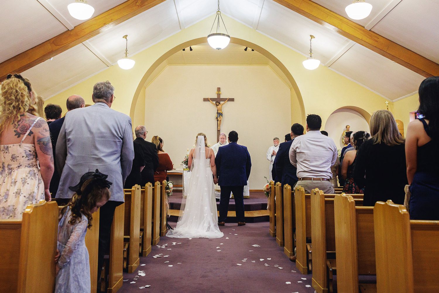 A bride and groom stand at the altar of a small church during their wedding ceremony, surrounded by seated guests.