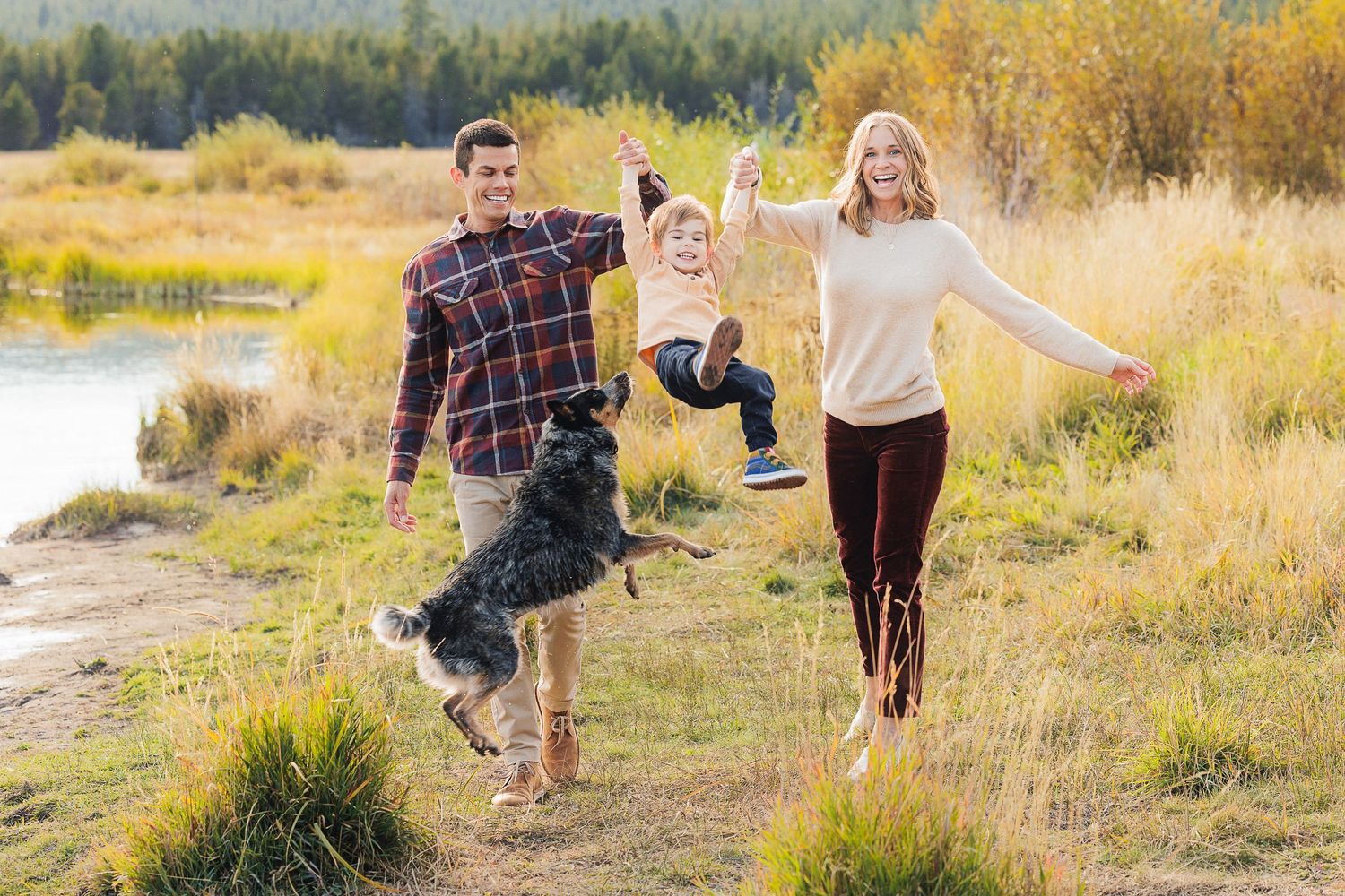 Family swinging child while walking together on path near lake.