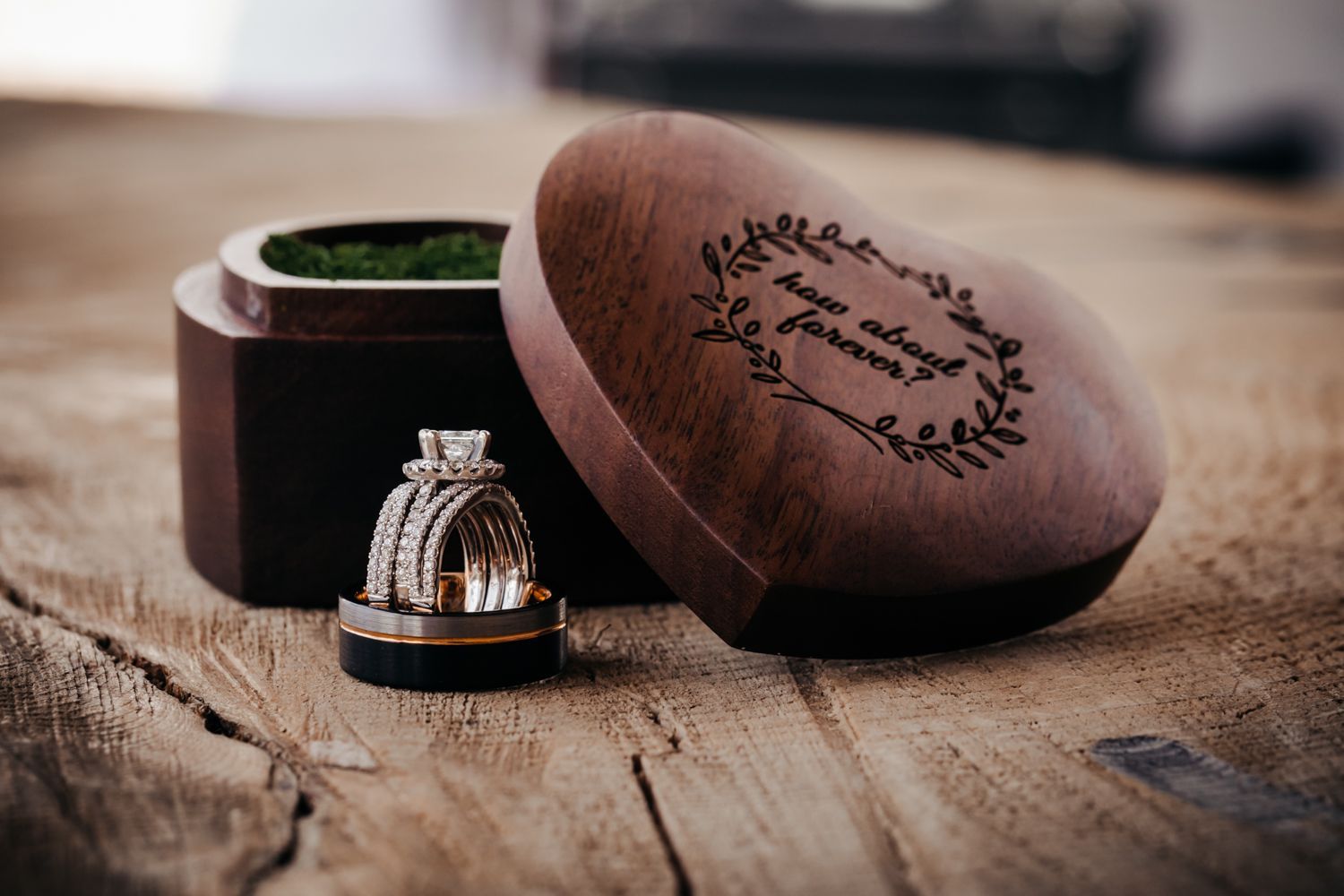 Wedding ring displayed next to a wooden ring box with custom engraving on rustic wooden surface.