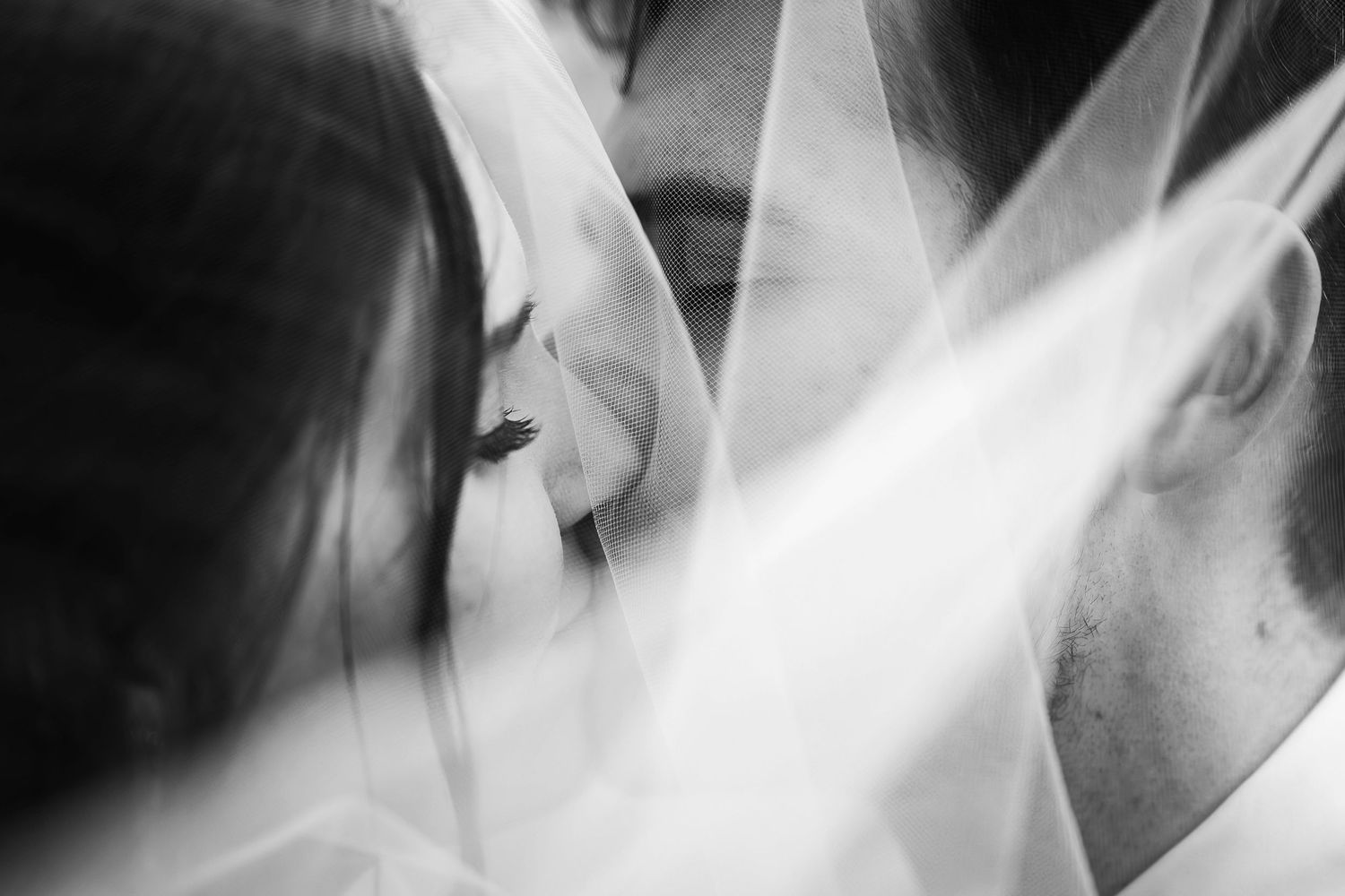 A black and white abstract photograph showing layers of ethereal white veils or fabric creating a soft, dreamy effect.
