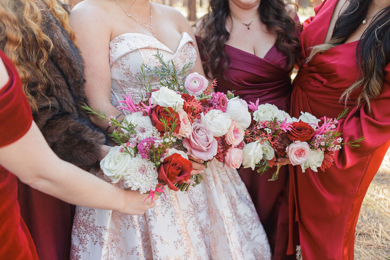 Close-up of wedding bouquets with pink and red roses held by bridesmaids in burgundy dresses.
