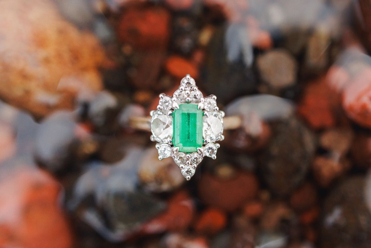 A close-up view of an emerald and diamond ring set in white gold or platinum against a blurred background.
