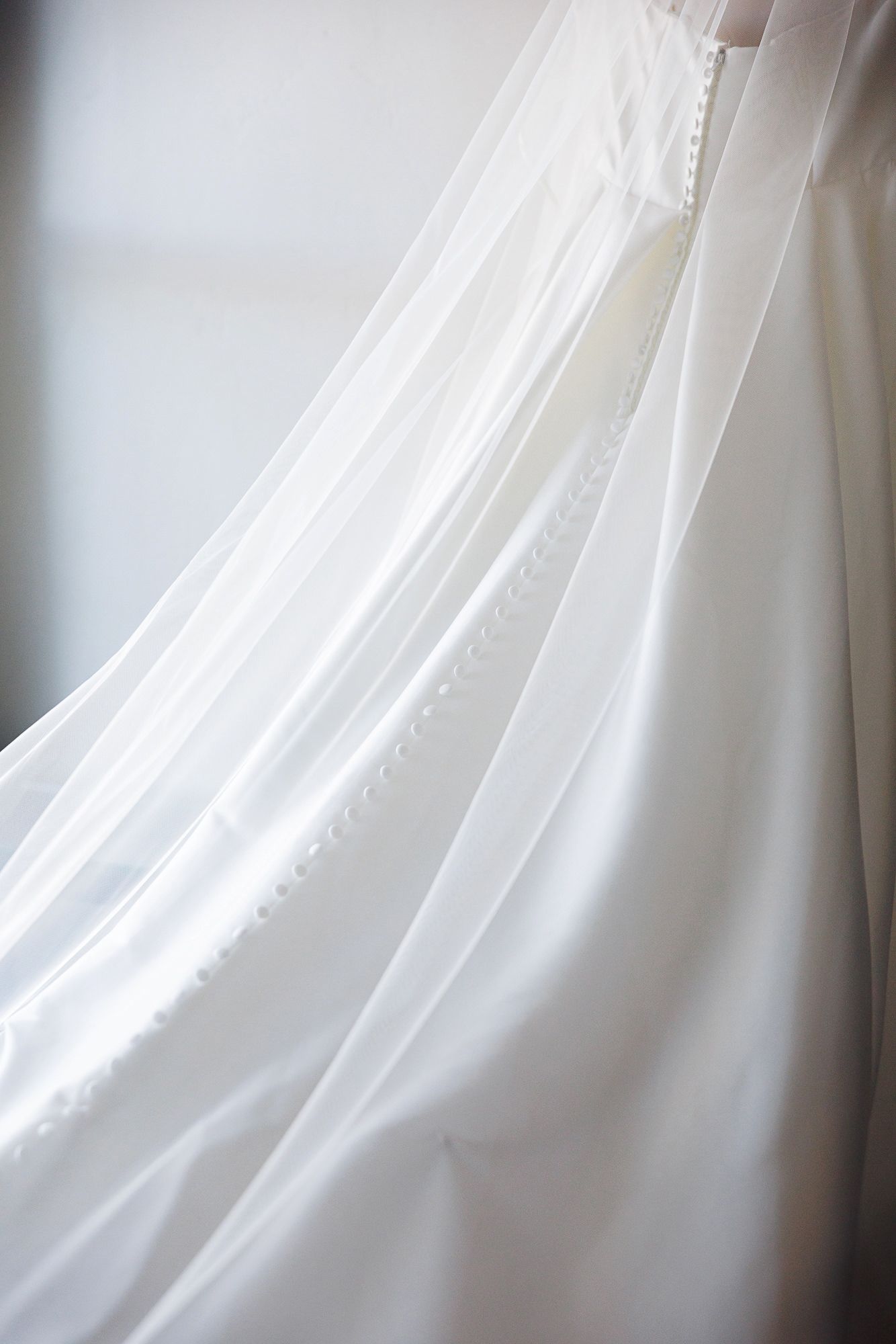 Close-up detail of flowing white wedding dress fabric with delicate draping and soft lighting.