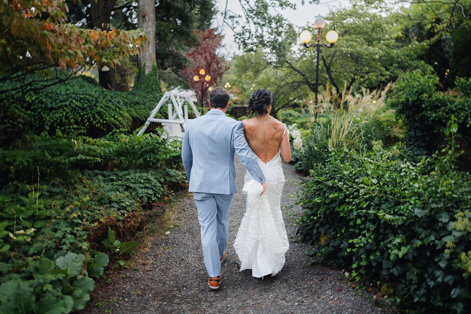 A couple walks along a garden path surrounded by lush greenery during their wedding celebration.