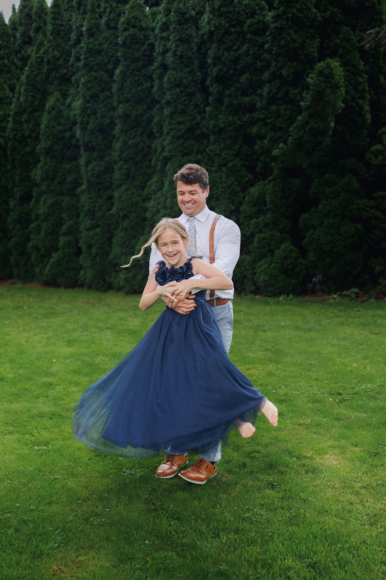 A playful dance sequence on a green lawn with a navy blue tulle dress twirling against evergreen trees in the background.