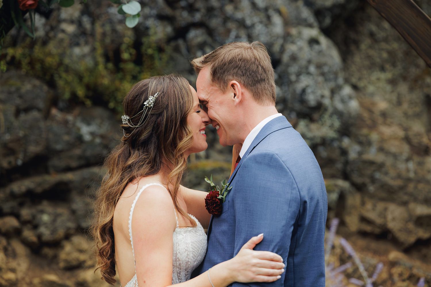 Couple shares intimate moments during outdoor photo session against rocky cliff backdrop.