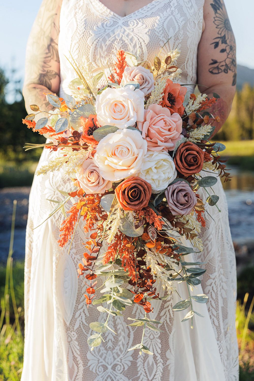 Beautiful wedding bouquet with blush pink and dusty rose flowers mixed with dried orange elements in golden sunlight.