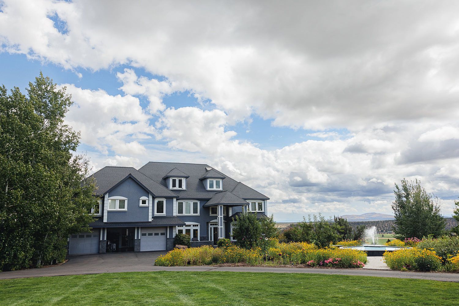 A panoramic photo sequence showing a modern gray house against a cloudy sky with surrounding lawn and trees.