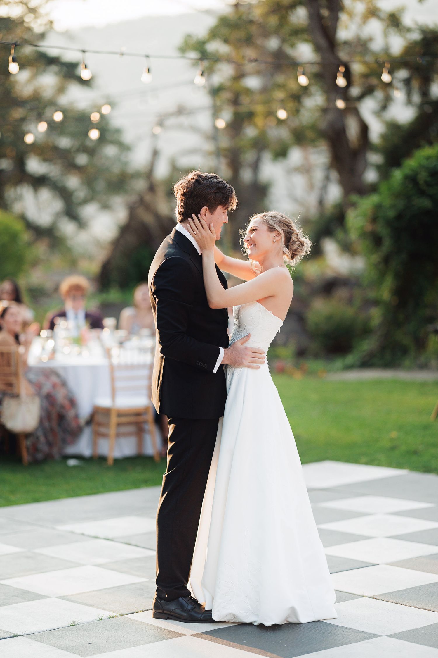 Bride and groom share first dance on checkered outdoor floor at elegant garden wedding reception.
