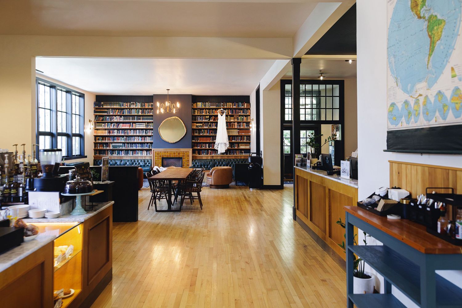 Cozy coffee shop interior with floor-to-ceiling bookshelves, hardwood floors, leather seating, and a world map on the wall.