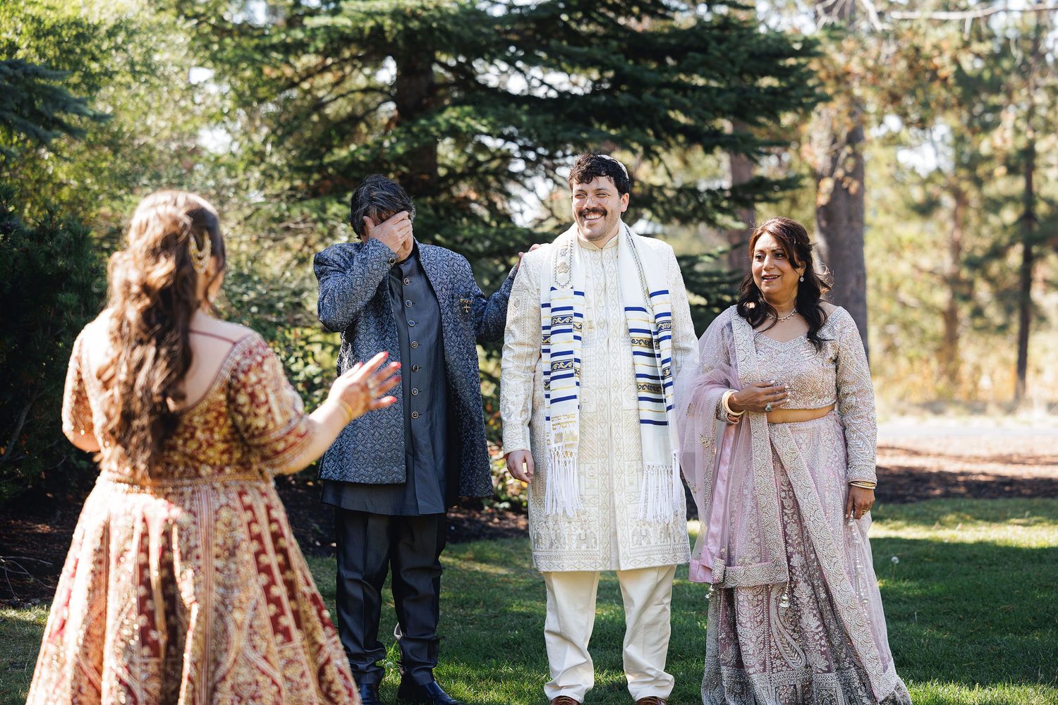 Indian wedding guests in traditional attire conversing outdoors in a lush garden setting.