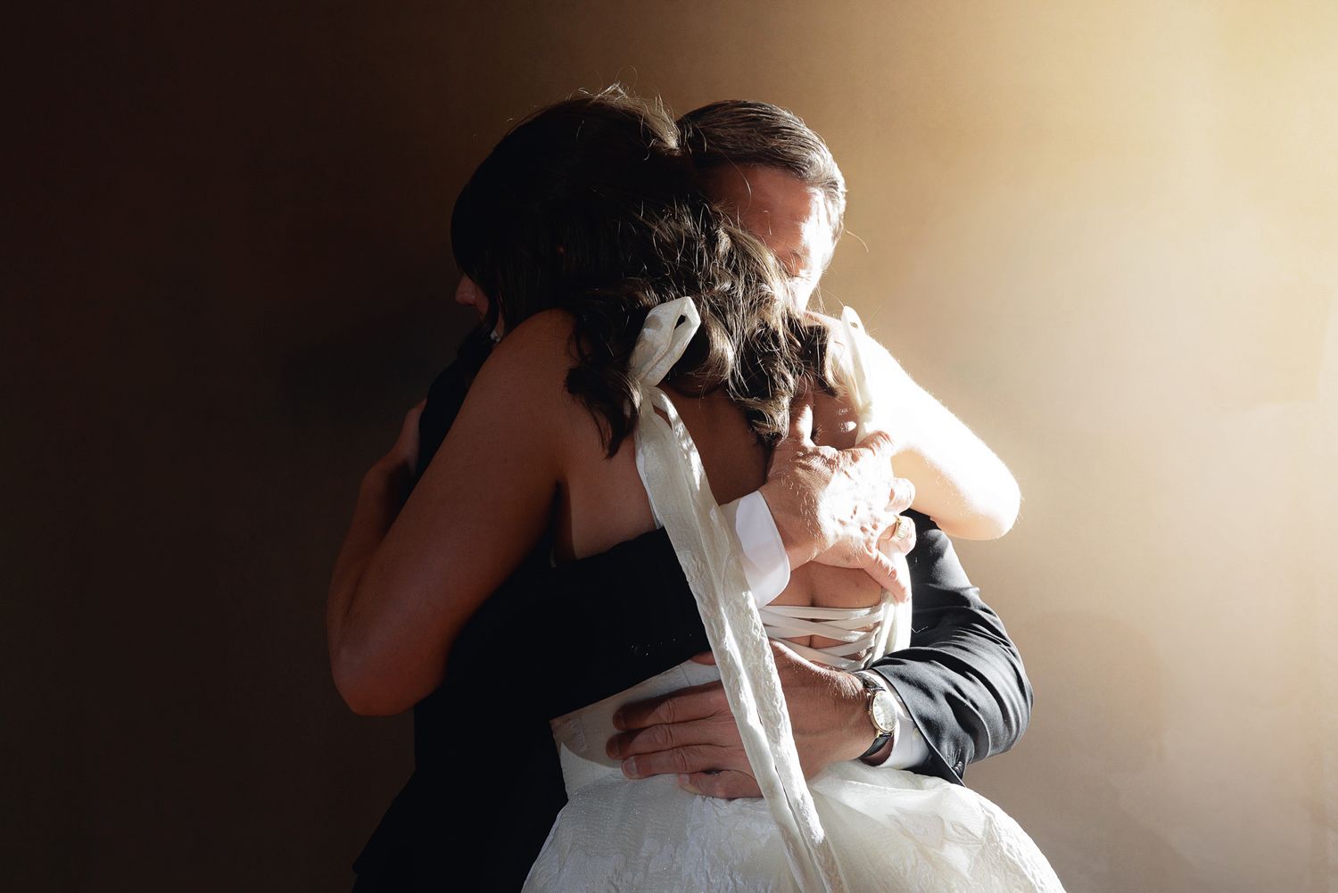 Bride and groom sharing an emotional embrace on their wedding day, captured in warm dramatic lighting.